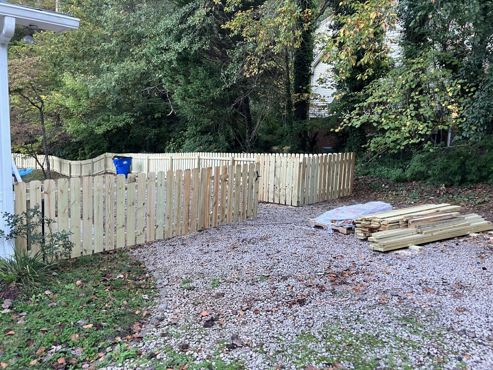 Wood picket fence installation along a gravel area