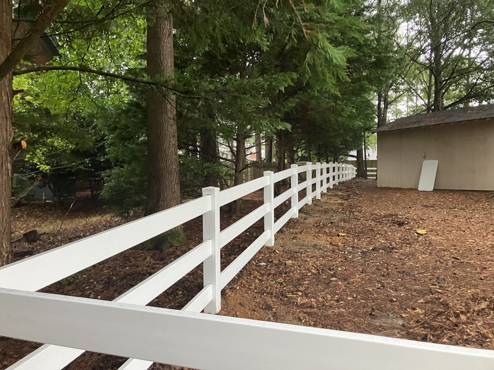 White three-rail vinyl fence along a wooded lot