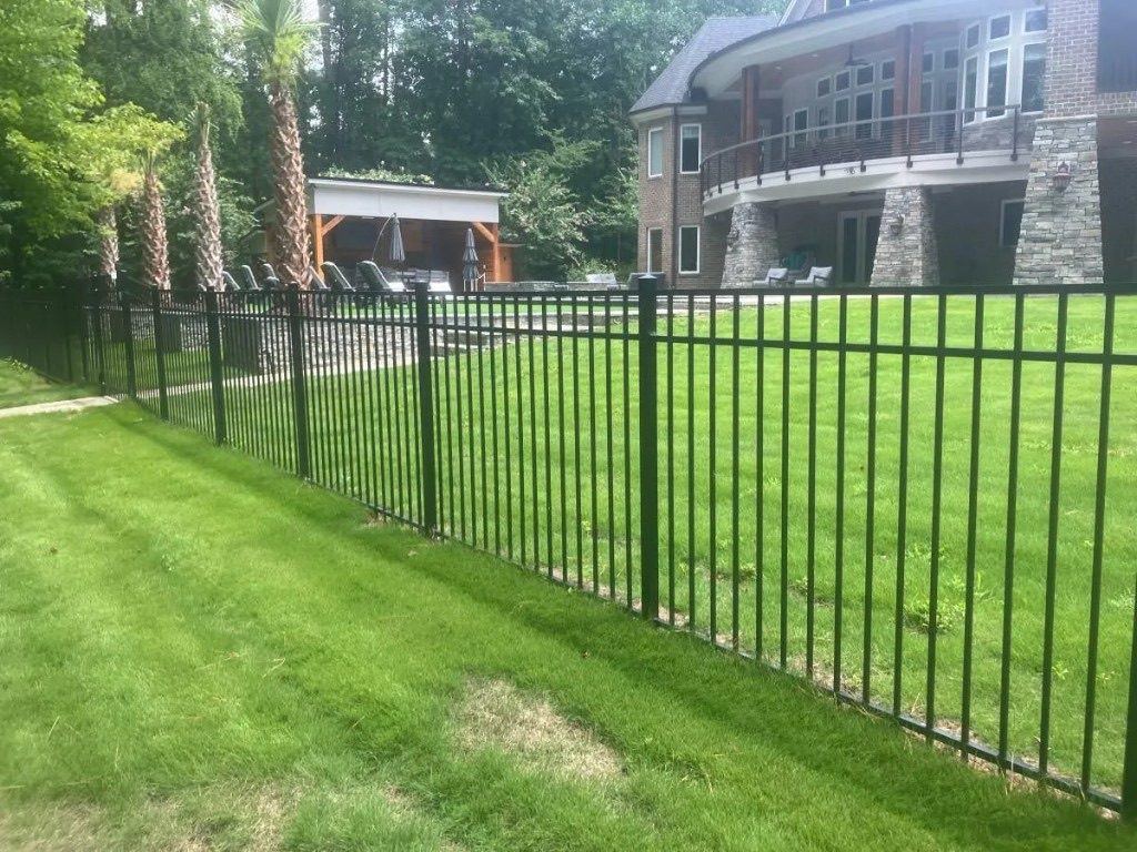 Black ornamental metal fence across a backyard lawn