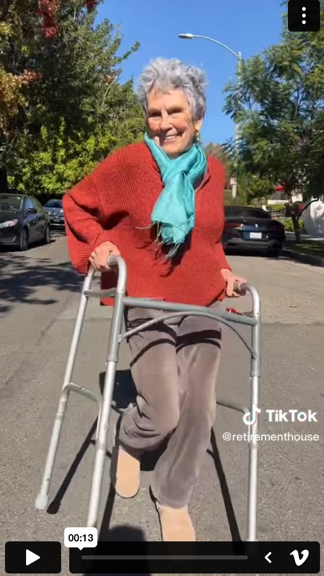 Gaylynn Baker walking with a walker in a red sweater and teal scarf