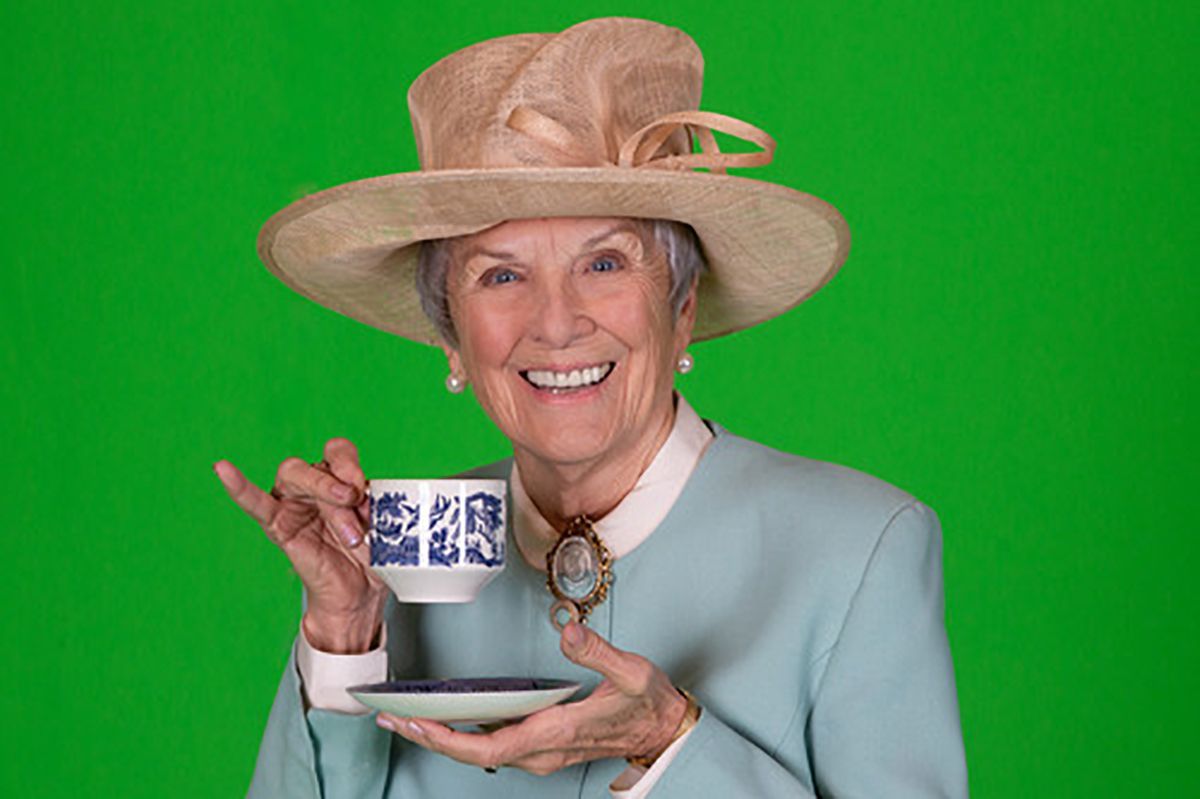 Woman in hat, holding teacup, smiling, against a green background.