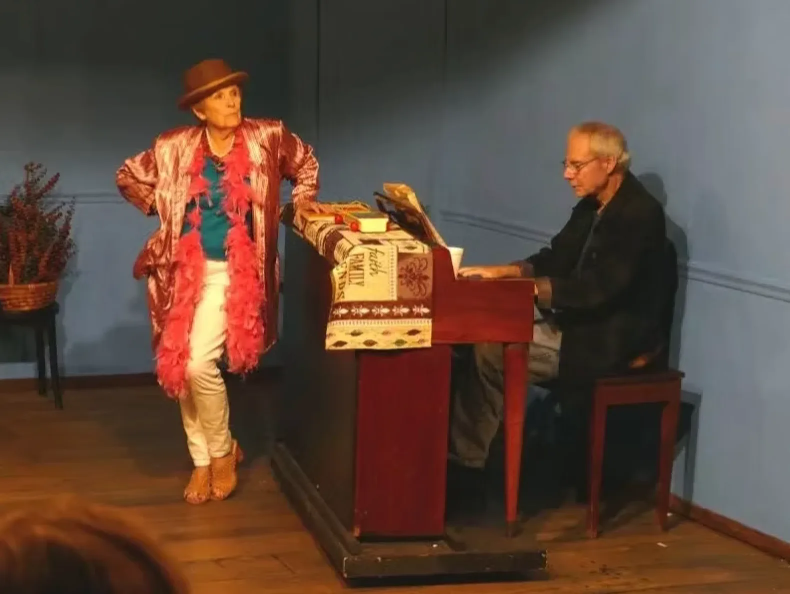 A woman in a boa and a man playing piano on a stage with a blue wall.